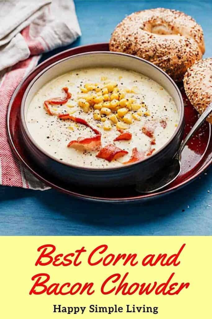 A bowl of corn and bacon chowder topped with bacon strips and corn sits on a red plate. A bagel is placed beside the bowl, and a spoon rests on the plate. Text reads Best Corn and Bacon Chowder with Happy Simple Living underneath.