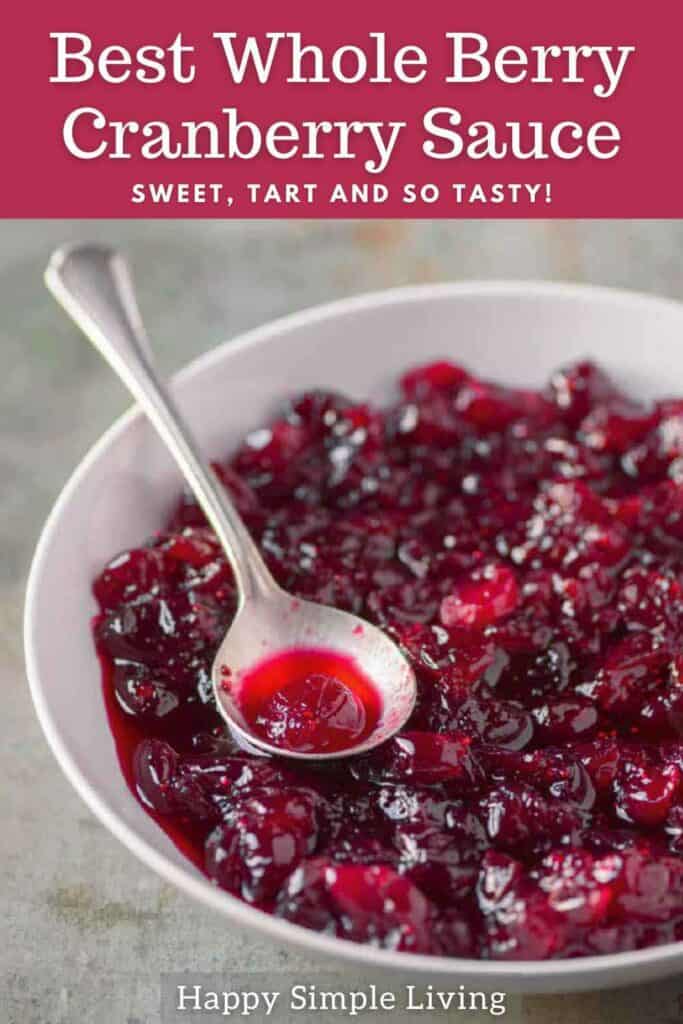 A bowl of whole berry cranberry sauce with a spoon, placed on a gray surface. The text reads Best Whole Berry Cranberry Sauce: Sweet, Tart, and So Tasty! and Happy Simple Living.