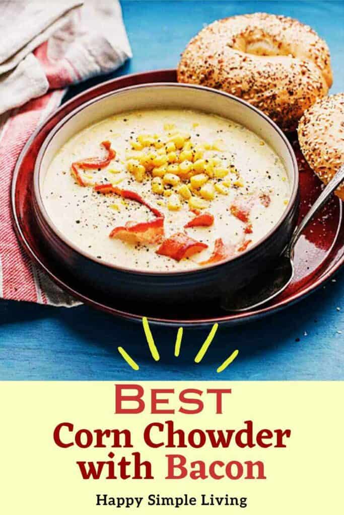 A bowl of corn chowder topped with bacon and corn sits on a red plate with a spoon. A bagel is on the side. Text at the bottom reads, Best Corn Chowder with Bacon - Happy Simple Living.